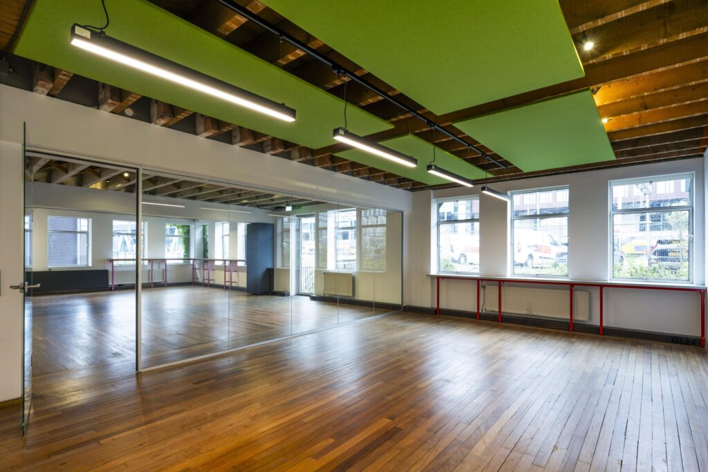 Lichte, moderne kantoorruimte aan de De Ruijterkade met houten vloer, glazen wand en groene akoestische panelen aan het plafond.